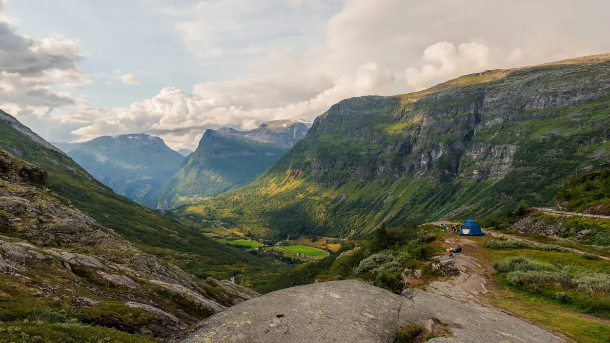 Sunlit green mountain valley with steep cliffs and dramatic passing clouds