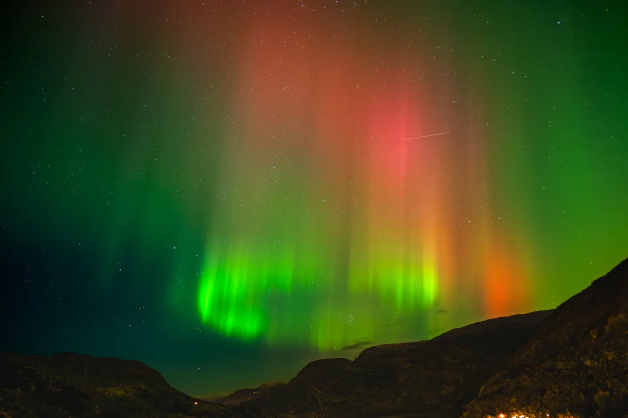 Bright green and red northern lights above dark mountain silhouettes and a star-filled sky